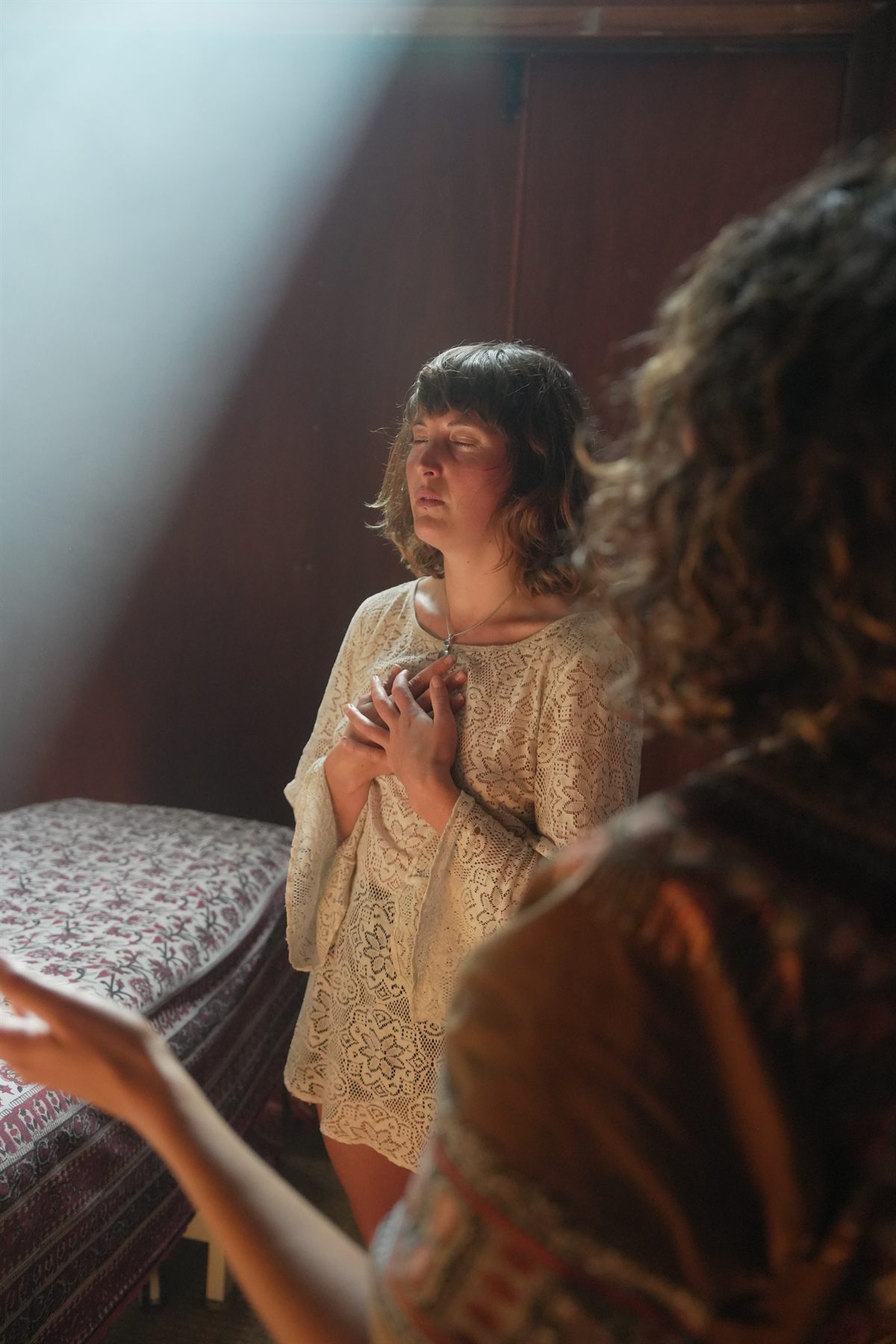 A client standing in prayer with hands on her heart during a healing session